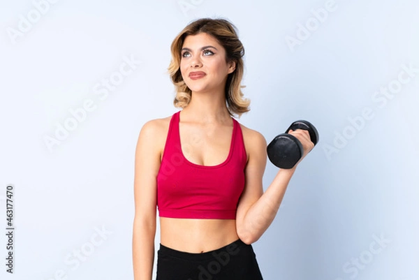 Fototapeta Teenager Russian girl making weightlifting isolated on blue background looking up while smiling