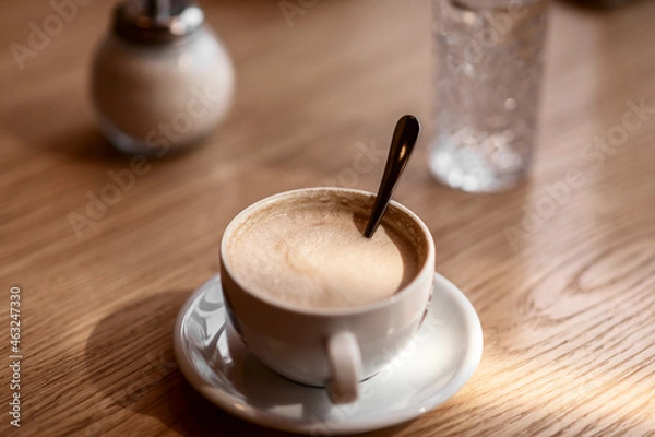Fototapeta a white cup of coffee on a wooden table in a cafe