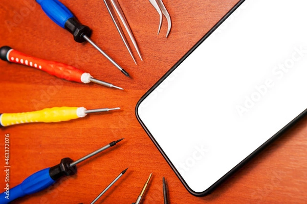 Fototapeta A mobile phone with an empty screen is lying on a table with repair tools, close-up, white screen.