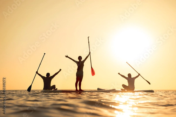 Obraz Happy surfers stands on sup boards with raised arms and looks at sunset
