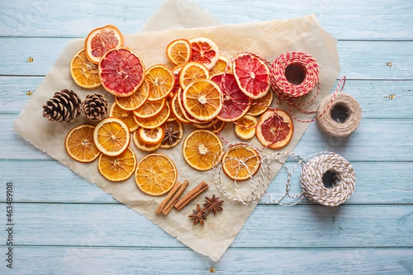 Fototapeta cinnamon, anise, dried oranges and grapefruit slices, threads for diy projects, gift wrapping and beautiful eco Christmas decorations like wreaths arranged on a blue wooden table