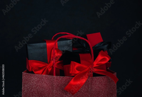 Fototapeta One red shiny bag with three gift boxes on a black background.