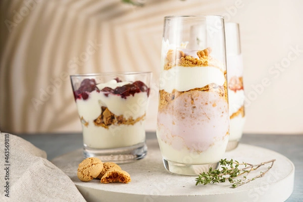 Fototapeta Three glasses with a layered creamy yoghurt dessert trifle with cookies, amaretti, cherries and thyme in a tropical setting