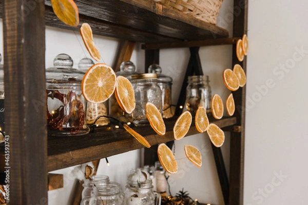 Fototapeta New Year's decor of the kitchen interior with an old wooden open shelf, with dishes and garlands of orange slices