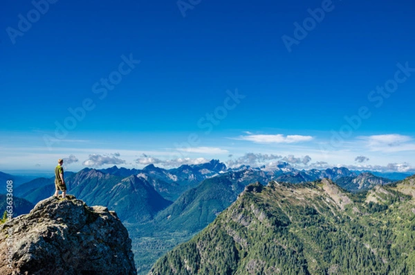 Fototapeta An athletic adventurous male hiker standing on top of a mountain looking out at a mountain range.