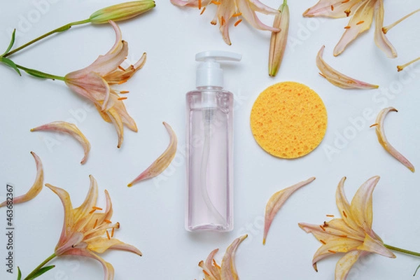 Fototapeta Transparent plastic cosmetic bottle with dispenser and pink gel on white background with a yellow sponge with a frame of yellow-pink flowers, petals and buds of lily flowers with empty space for text