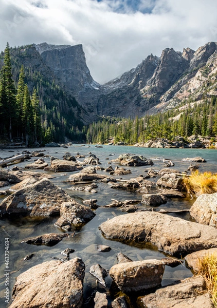Fototapeta View of dream lake surrounded by mountains in rocky mountain national park, colorado. The lake has many rocks and the peak of the mountain is pointed and surrounded by trees.