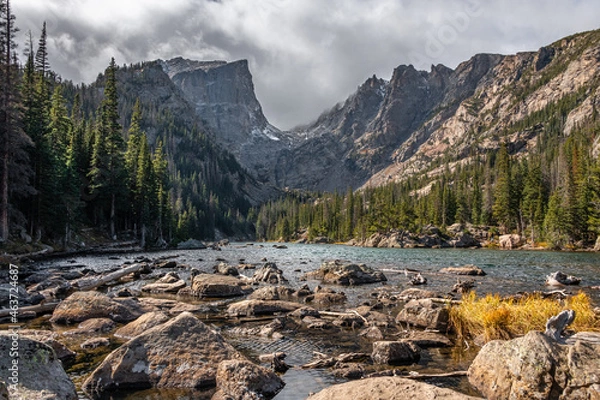 Fototapeta View of dream lake surrounded by mountains in rocky mountain national park, colorado. The lake has many rocks and the peak of the mountain is pointed and surrounded by trees.
