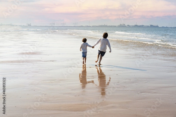 Obraz Two happy brothers holding hands are running along the seashore at the North Sea. Boys spending weekend at the  seaside in Belgium, Knokke. Siblings friendship concept.