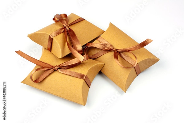 Fototapeta Small gifts in a box made of natural cardboard. The craft box is tied with a brown satin ribbon. Group of gifts, copy space. Gift boxes with recycled paper on white.
