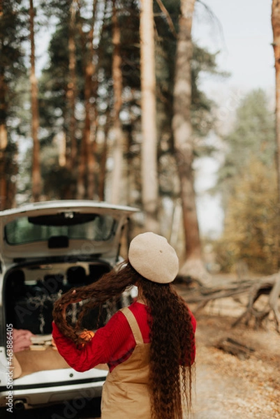Fototapeta girl with long hair and a white beret stands in the autumn forest against the backdrop of a large car