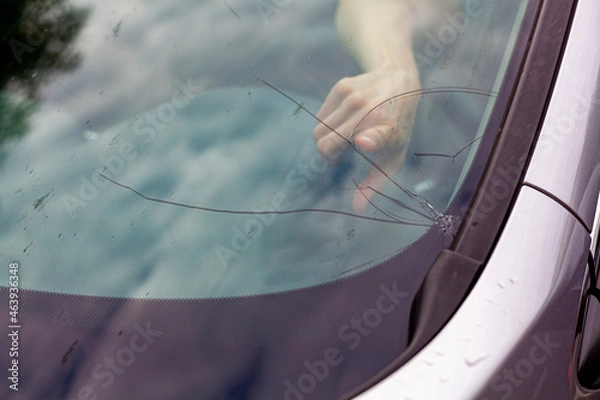 Obraz Cracked front windshield after stone chip on the road. Driver points out the place of impact. A costly repair covered by comprehensive car insurance.