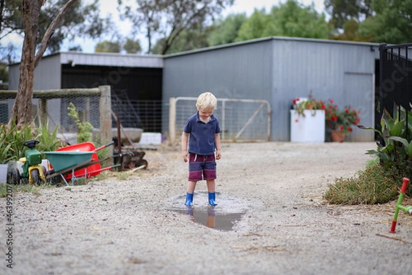 Fototapeta Little boy wearing gum boots jumping and splashing in puddle