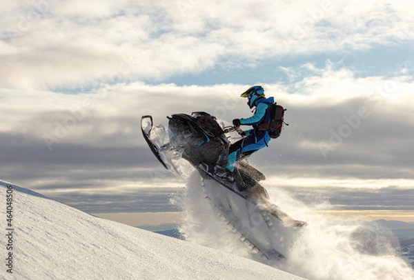 Obraz snowmobiler jumps in a bright helmet and overalls over a mountain valley after a snowfall on a frosty morning. snowmobile sports concept