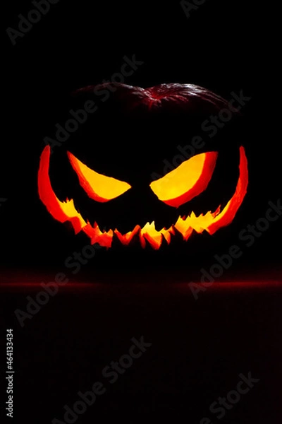 Fototapeta Jack o' lantern in a spotlight glow on a dark  background. Halloween pumpkin with an evil smile