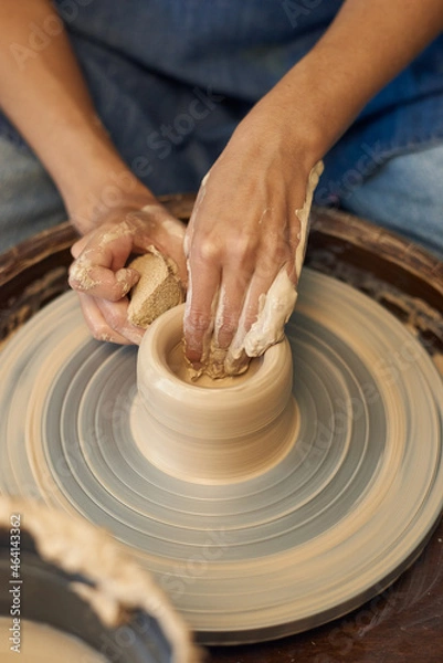 Fototapeta Close-up of unrecognizable potter working with clay on pottery wheel and removing water stains from pot with sponge