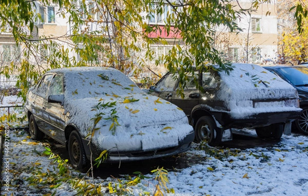 Fototapeta a passenger sedan parked in the parking lot was covered with snow and branches during a severe snowstorm in late autumn. fuzzy focus