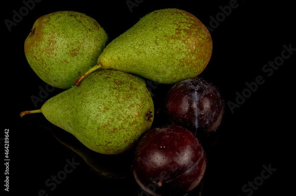 Fototapeta Fresh and wet pears and plums on a black background. Water drops on fruits