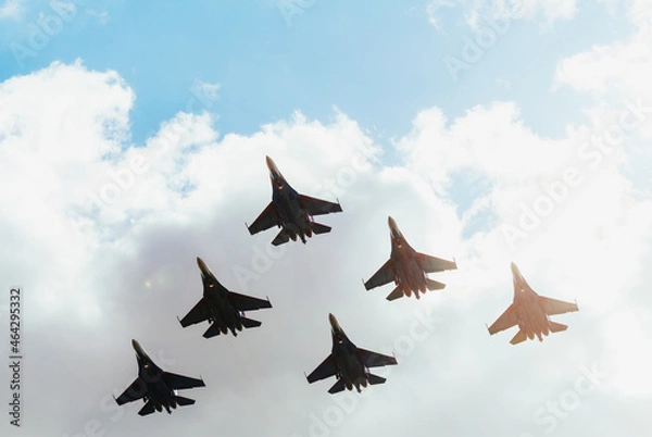 Fototapeta A squadron of jet soldiers, fighters, and airplanes perform a maneuver against the background of a blue and cloudy sky.