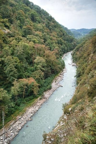 Fototapeta Panorama of the mountain gorge. A clear mountain river deep below. The forest covers the mountains around.
