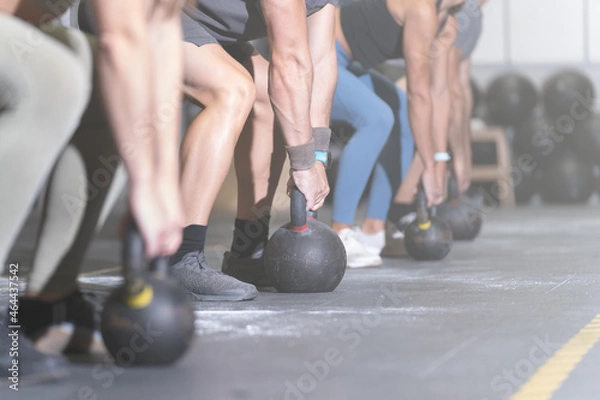 Fototapeta Group of faceless athletes working out with kettlebells in a cross training center