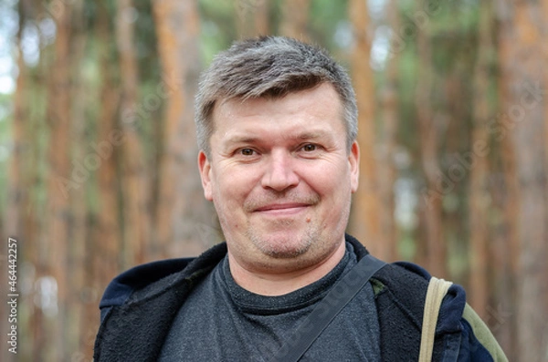 Fototapeta Portrait of a positive middle-aged man in front of a blur of tal