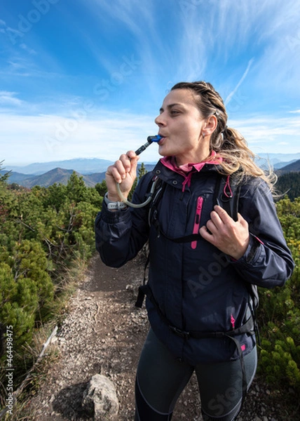 Fototapeta Woman tourist drinks water through a hose from a camelbak while walking. 