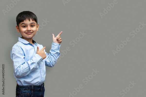 Fototapeta Smiling happy boy pointing finger away at copy space isolated over plain background