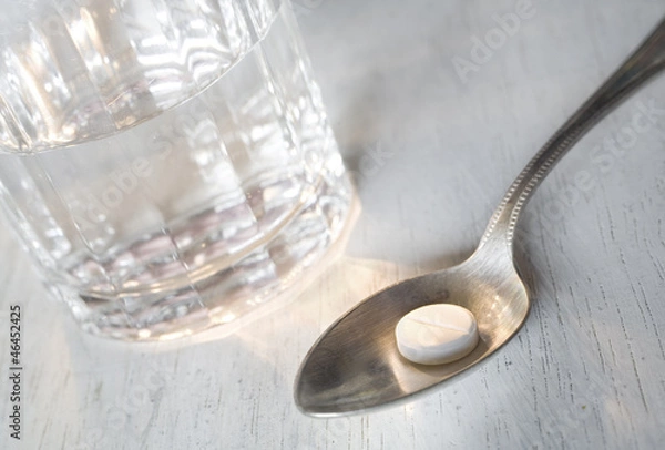 Fototapeta Pill on a spoon with a glass of water