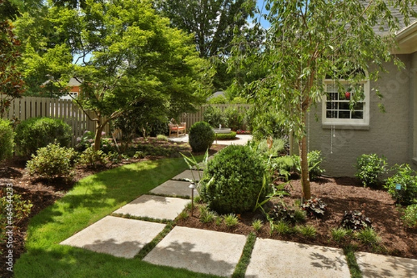Fototapeta Stone path through backyard garden with bushes and trees