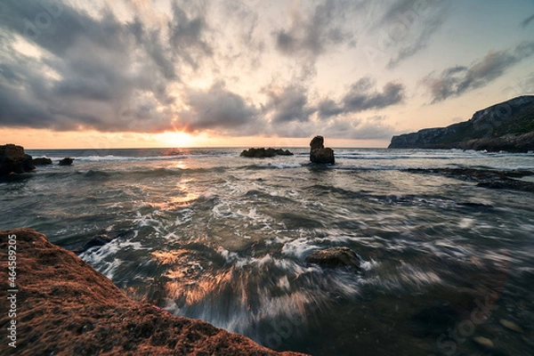 Fototapeta Sunrise at the touristic beach Las Rotas in Denia,  Spain in a cloudy day. There are strong tides and waves. It's a very visited beach at the marine reserve of San Antonio Cape in Alicante