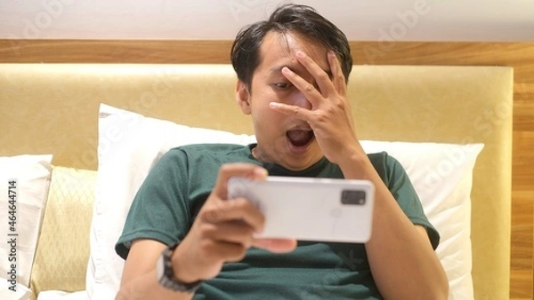 Fototapeta Shocked and surprised funny face of Asian man watch the smartphone alone at night.