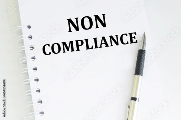 Fototapeta text NON COMPLIANCE on a white notebook next to the handle on a light table
