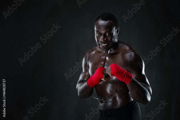 Fototapeta African american athletic fighter demonstrating boxing stance, raising fists up, black background, copy space