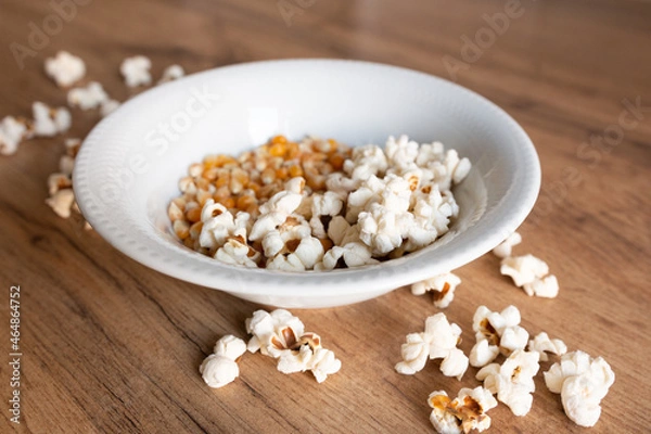 Fototapeta Fried popcorn and beans lies in a white plate and scattered a row on a wooden table