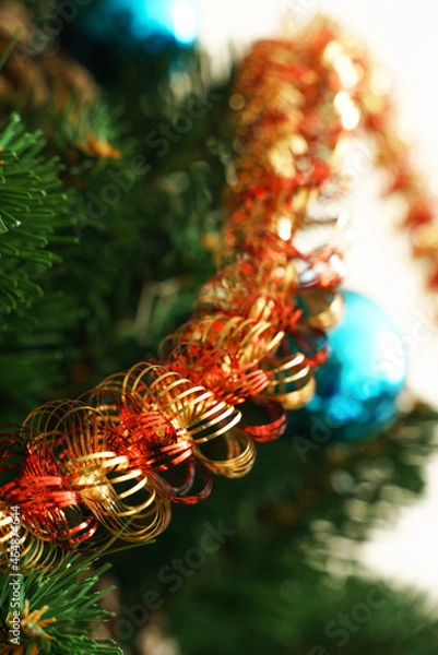 Fototapeta Golden-red tinsel against the background of green branches and needles of an artificial Christmas tree