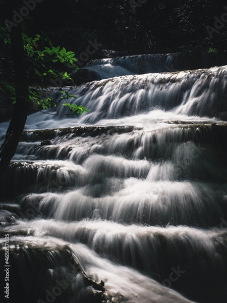 Fototapeta Scenic view of Erawan Waterfall. Breathtaking smooth flowing white water stream closeup with sunlight in lush rainforest. Kanchanaburi, Thailand. Minimal long exposure.
