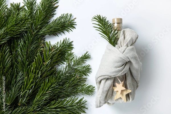 Obraz Zero waste Merry Christmas winter gift wrapping, bottle in Japanese furoshiki style in linen fabric, decorated with natural green branches of fir nobilis. Concept eco-friendly creative package