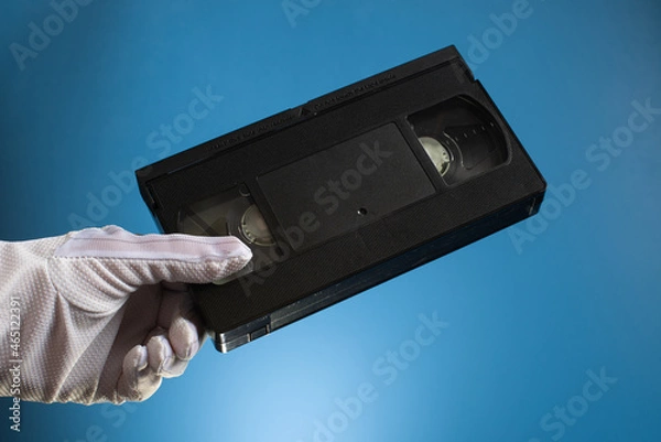 Fototapeta Hand holds retro HVS video cassette on a blue background. Retro wave. 80s 90s