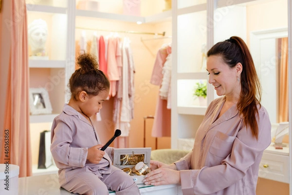 Obraz caucasian mother and African-American daughter in pink pajamas in the dressing room and bedroom playing with makeup