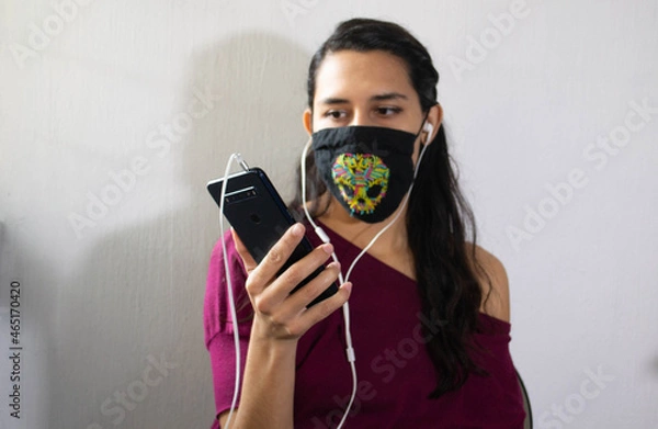 Obraz Mujer con teléfono celular, audifonos y cubreboca de calavera