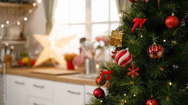 Fototapeta kitchen at Christmas time in bright modern home interior. focus view on xmas tree in side with blurred back view of cooking place in apartment. red and gold balls decorations hanging on tree
