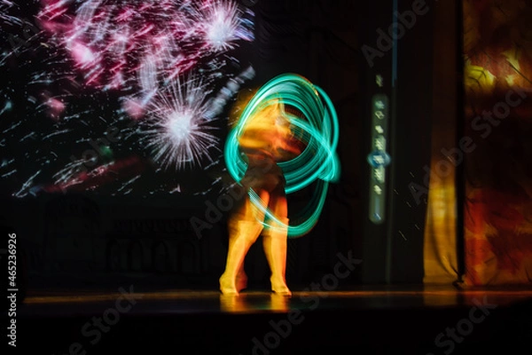 Fototapeta an artist on stage with glowing hoops. a girl in an LED suit performs in a bright show in the dark. the multicolored hula hoop glows. dancing and gymnastics
