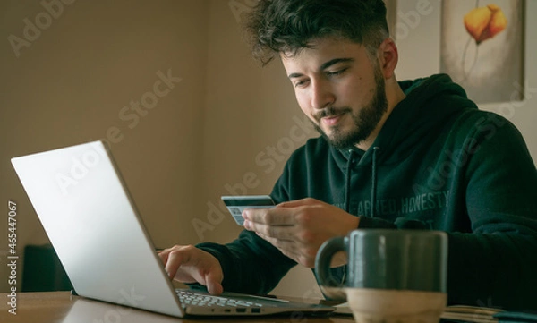 Fototapeta young man making online purchases with a card in front of a laptop