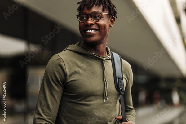 Obraz Happy successful african student, wearing glasses and with a black backpack, standing on the steps and smiling