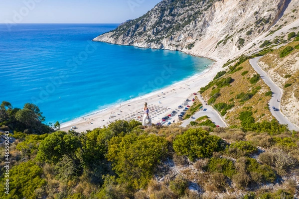 Fototapeta Happy woman standing on top of a rock with hat enjoying Myrtos Beach. Cephalonia island, Greece