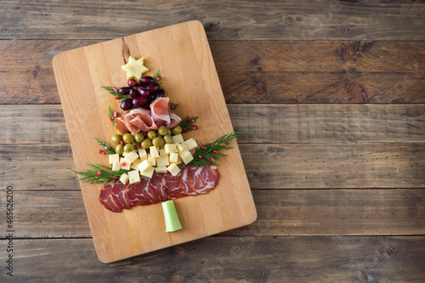 Fototapeta Christmas tree shaped cheese and charcuterie board with wooden background. Top view. Copy space.