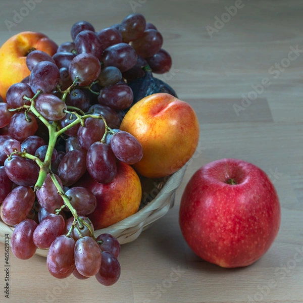 Fototapeta red grape berries and fresh fruits in a straw basket on a light wooden background