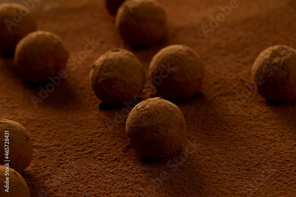 Fototapeta Truffles with cocoa, coconut and sesame seeds with chocolate with cocoa powder, delicious dessert under dramatic lighting
