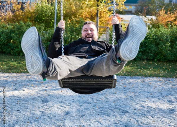 Fototapeta adult bearded man rides a child's swing and laughs